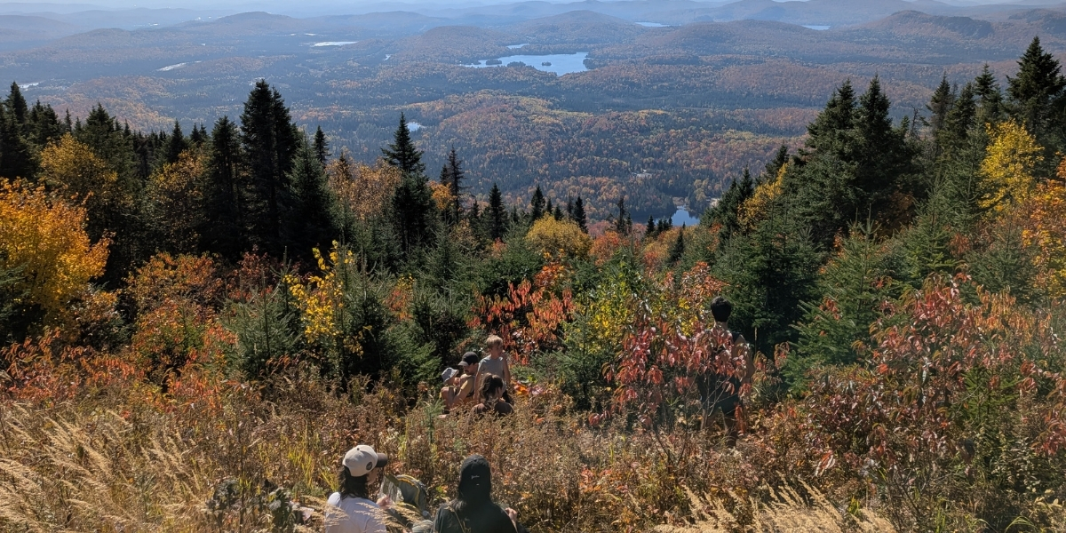 00Feature image_MEC Laval story_credit Marc-André Aubin | Sentier Transcanadien two people sitting at hike lookout over fall foliage and lakes below