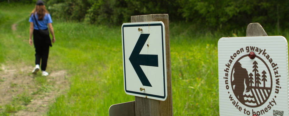 trail signage behind a woman walking in a field