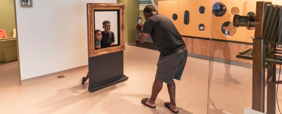 04Support image_TWEPI article_Chimzuk Museum_credit Tourism Windsor Essex Pelee Island | Sentier Transcanadien man taking a photo of kids in a photo frame at museum