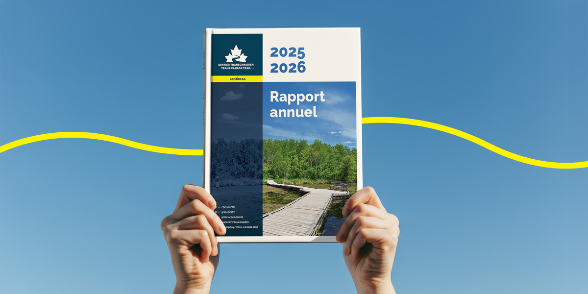 Annual report cover for 2025–2026 with a boardwalk image and blue sky background, held up by hands