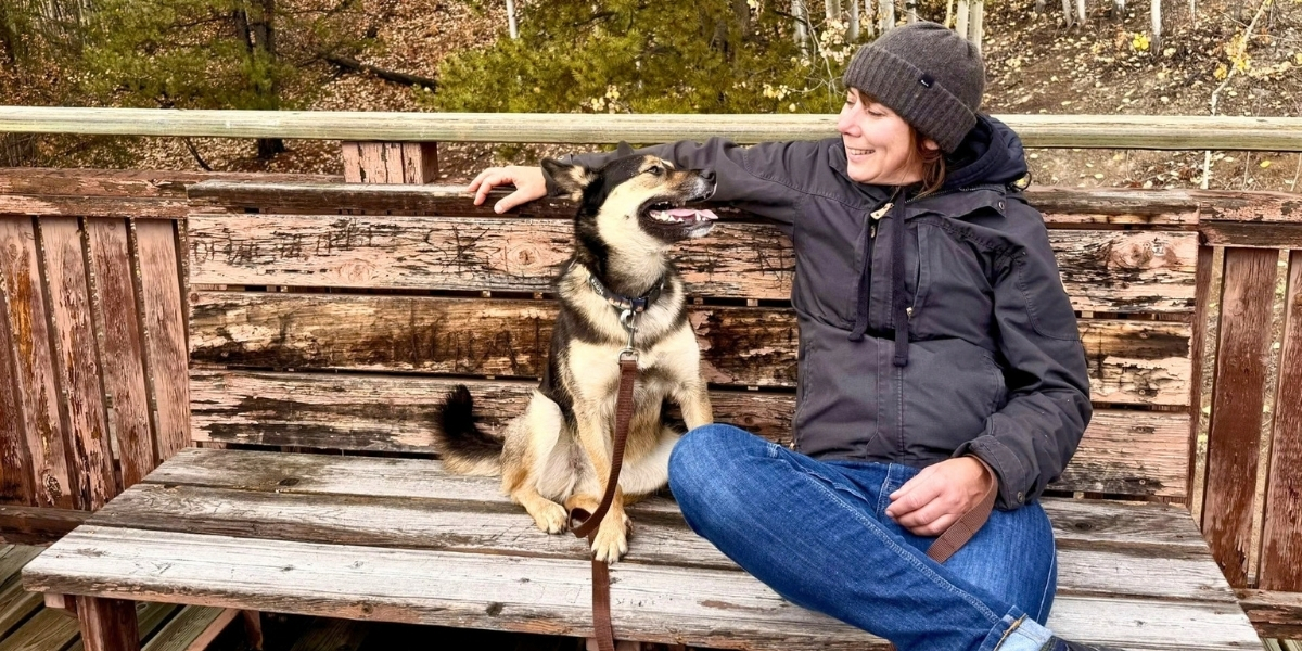 00Feature image_Mel Vogel GCH profile_photo credit Mel Vogel | Sentier Transcanadien A woman and her dog sitting on a bench, looking at one another