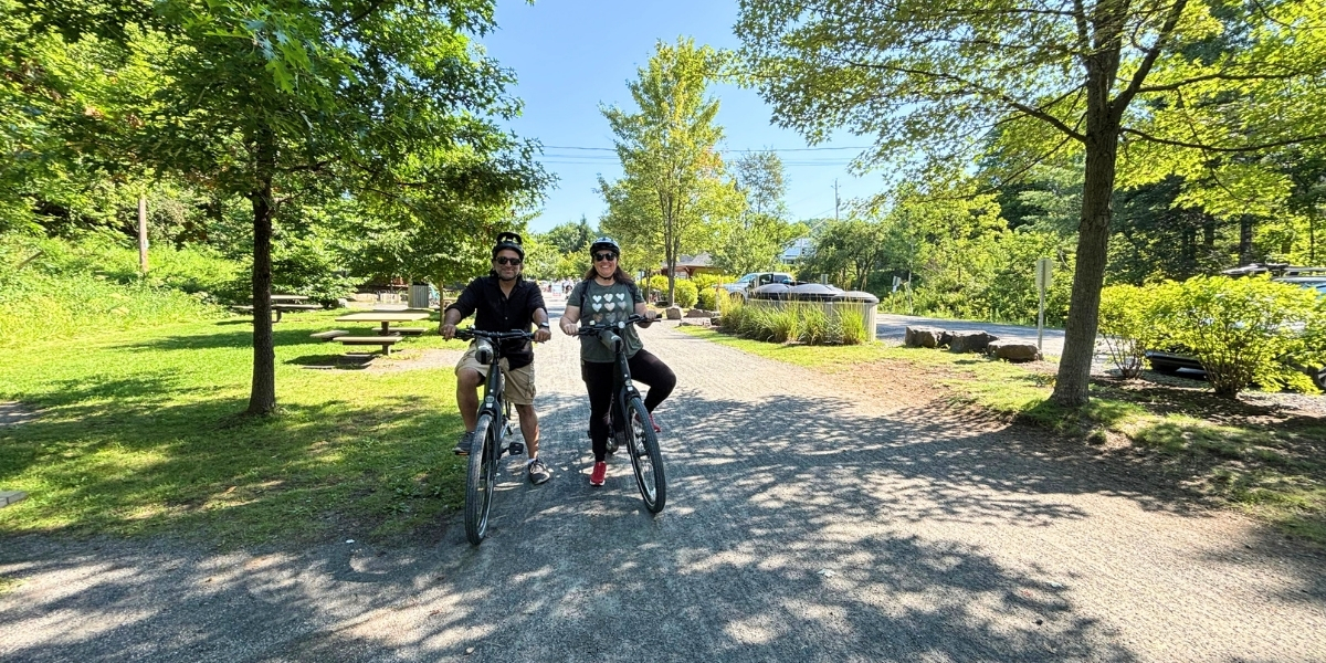 Two people with their bikes on a gravel trail. There are green trees on either side.
