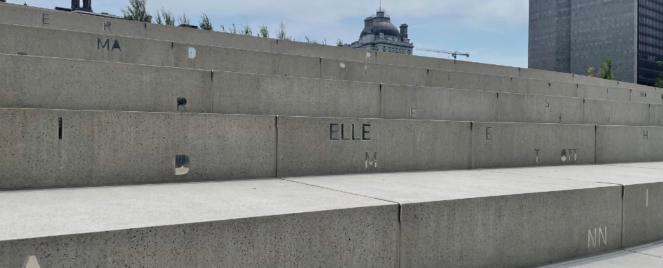 Tiered concrete steps in an outdoor plaza with scattered letters on the blocks; the word 'ELLE' visible in the center, with city buildings in the background.
